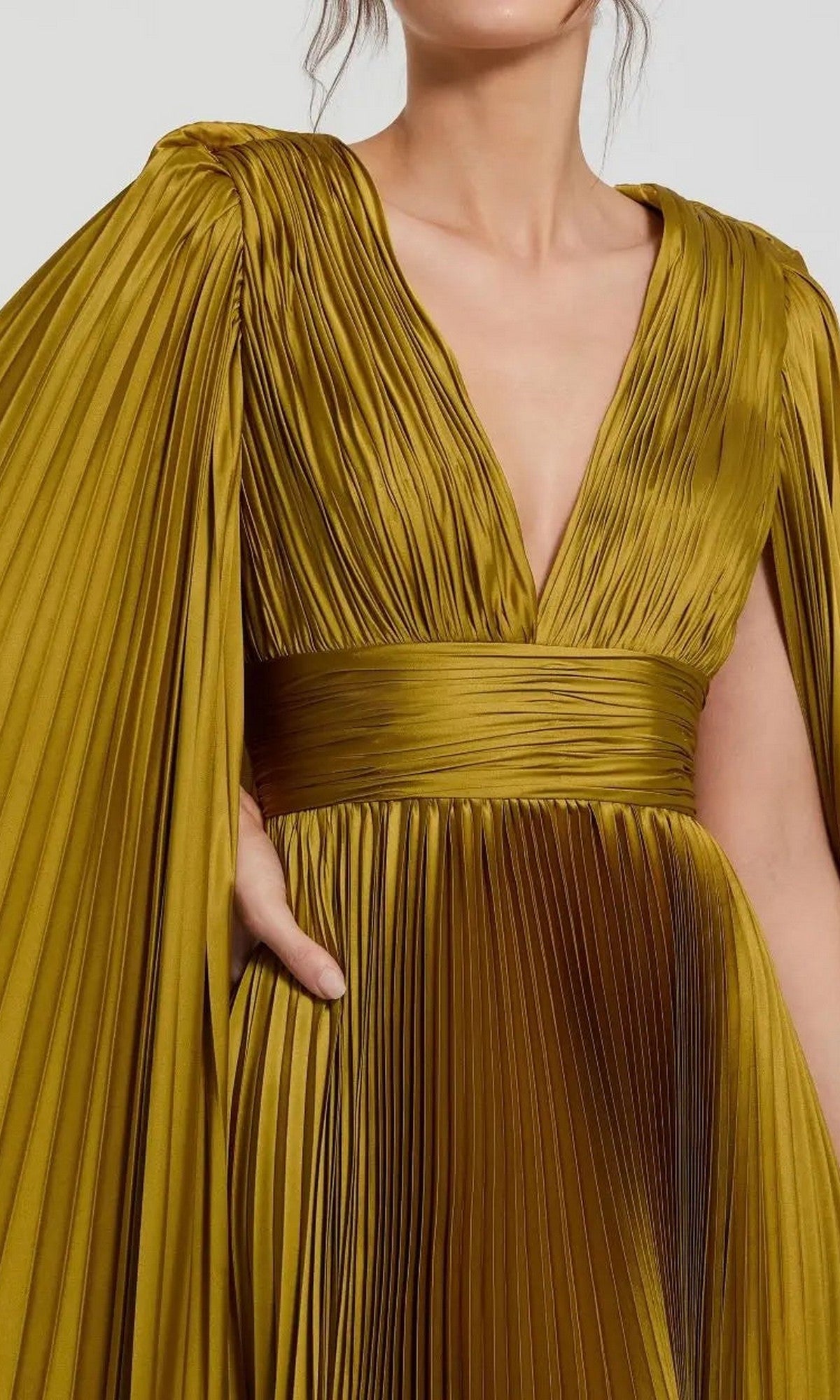 A woman wears the Mac Duggal 49872 long formal dress—gold charmeuse with a deep V-neckline, wide waistband, and dramatic pleated cape sleeves.